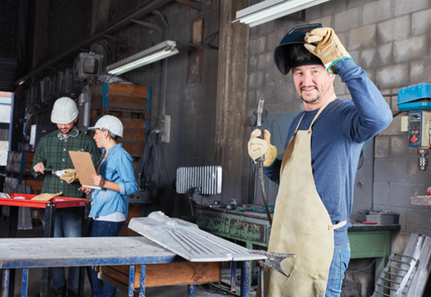 A man in a factory wearing an apron and hard hat, ready to work and ensure safety in the industrial setting.