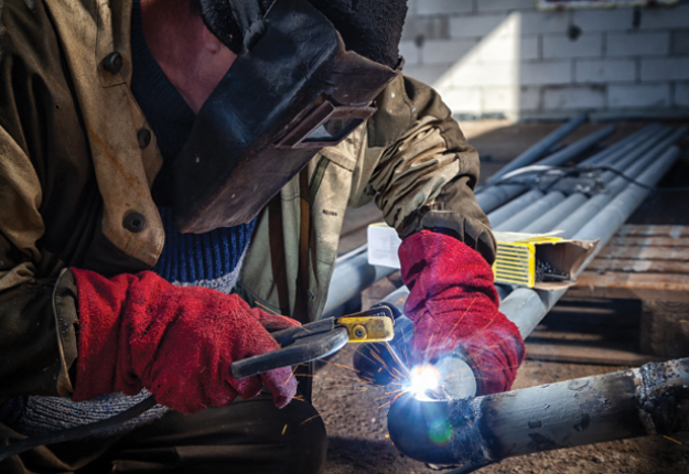 A man in a welding helmet welding a metal pipe.