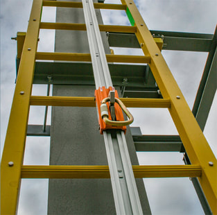 hero-vertical-climbing-system A closeup of a Ladder Fall Arrest System, which consists of a carabiner on a rail in the middle of a ladder.
